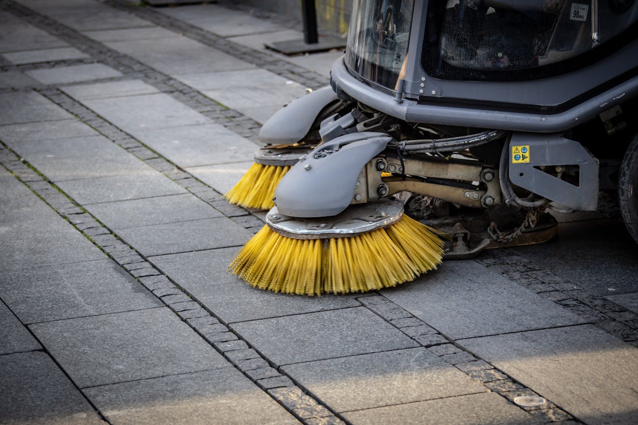 Close-up view of a road sweeper's yellow brushes on a paved street.