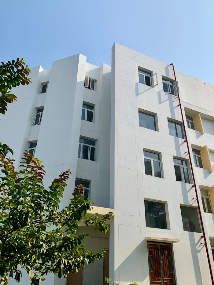 Contemporary white apartment building facade with glass windows and leafy foreground.